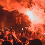 Political Risk - Crowd of unrecognizable activists with burning torches standing on street among smoke during demonstrations at night