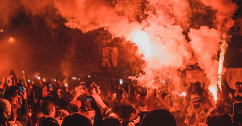 Political Risk - Crowd of unrecognizable activists with burning torches standing on street among smoke during demonstrations at night