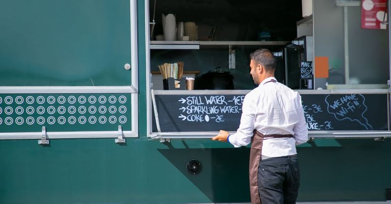 Sales Process - Back view of male seller wearing apron preparing food truck with menu written on board