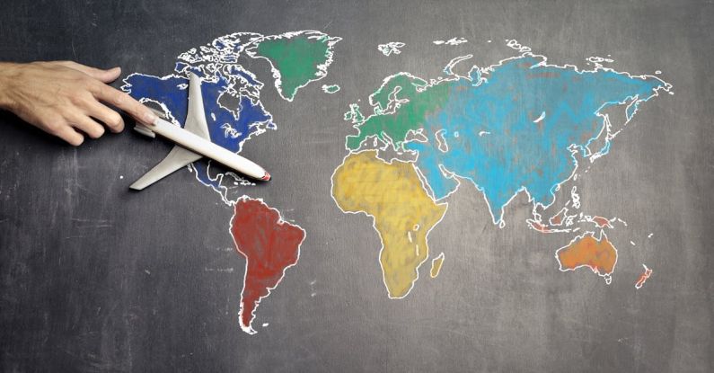 Globalization - Top view of crop anonymous person holding toy airplane on colorful world map drawn on chalkboard