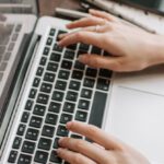 Employee Turnover - From above of unrecognizable woman sitting at table and typing on keyboard of computer during remote work in modern workspace